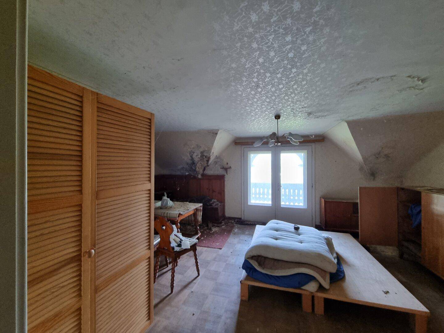 Schlafzimmer im Dachgeschoss mit Holzschrank, Bett und Fenster, renovierungsbedürftig.