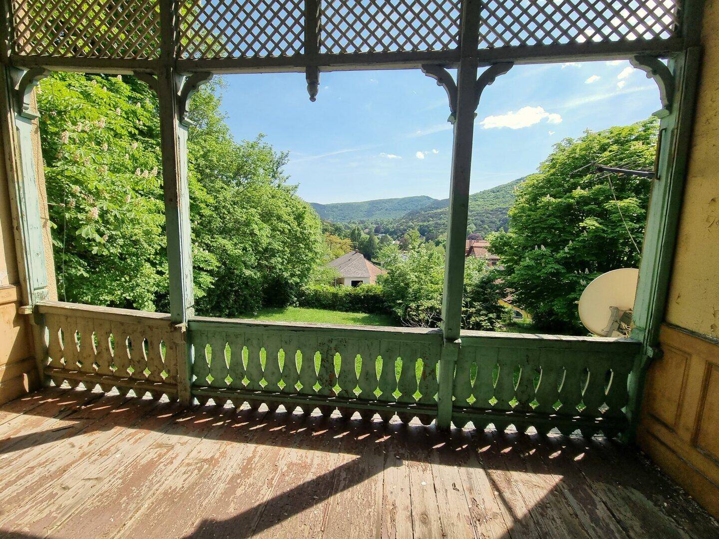 Alter Balkon mit Holzboden und Gittergeländer, bietet einen weiten Blick ins Grüne.