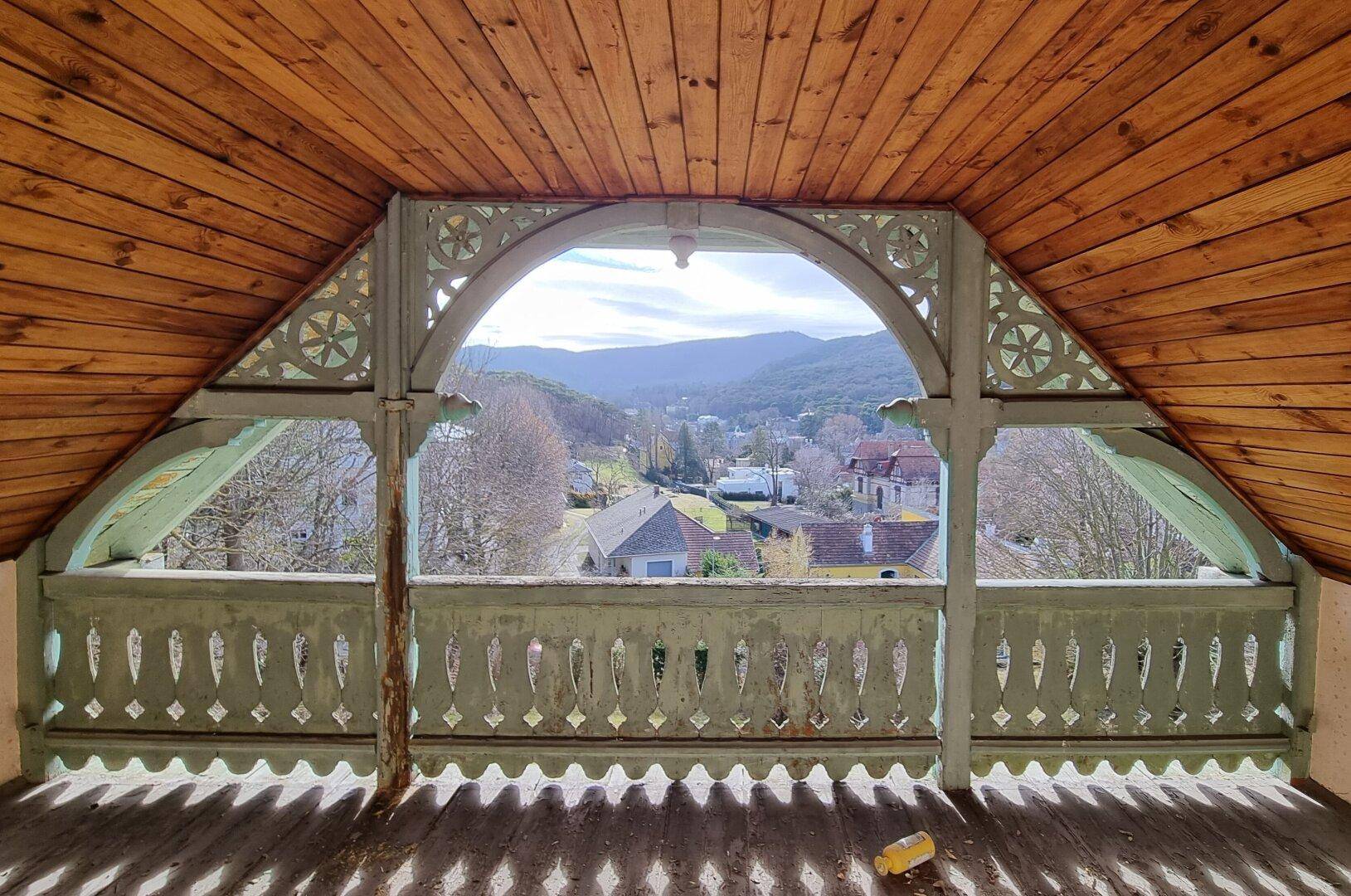 Dachgeschoss mit Holzbalken und weitem Blick ins Tal von einem überdachten Balkon.