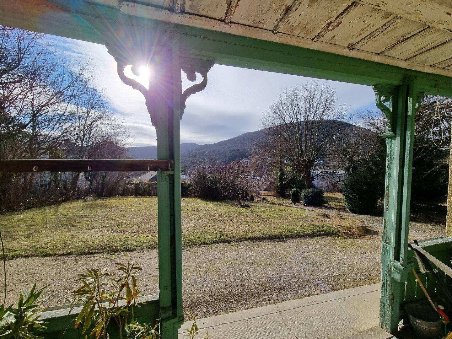 Überdachte Terrasse mit Blick auf den Garten und die umliegende Landschaft, sonnig.