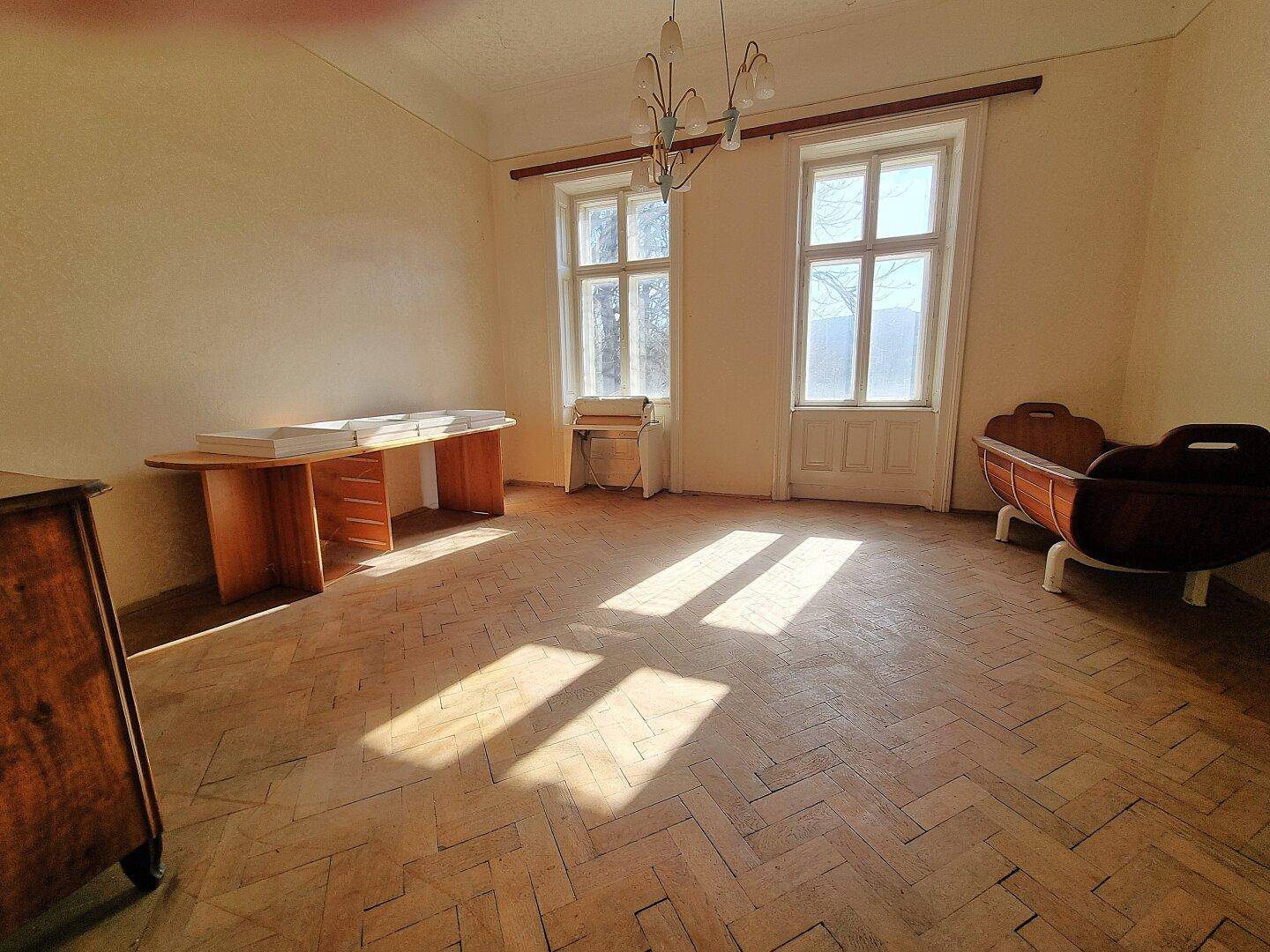 Helles Zimmer mit Fischgrätparkett, hohen Fenstern und Sonnenlicht, unmöbliert und geräumig.