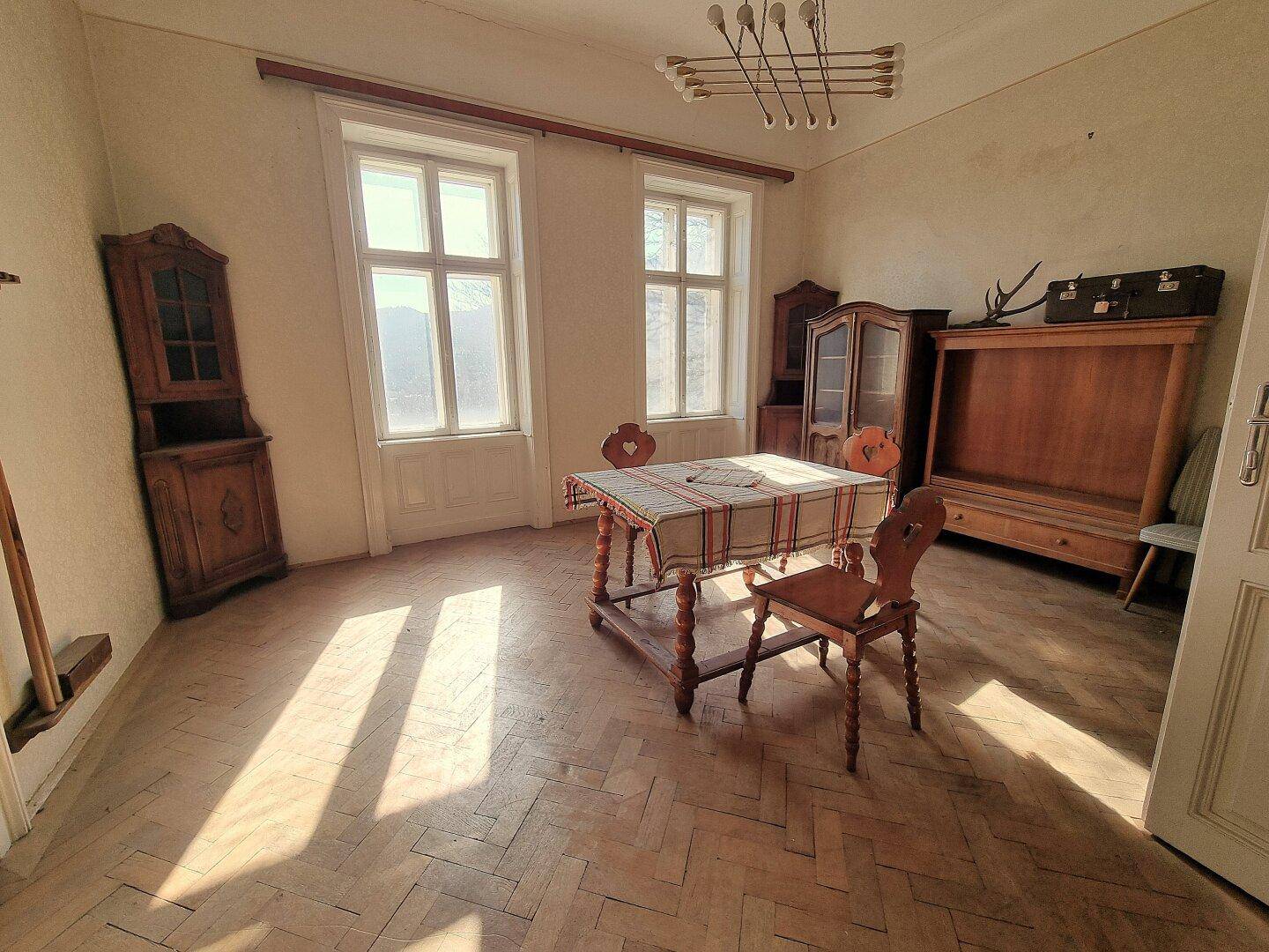 Traditionelles Esszimmer mit Holztisch, Stühlen und Schränken, hell durch große Fenster.