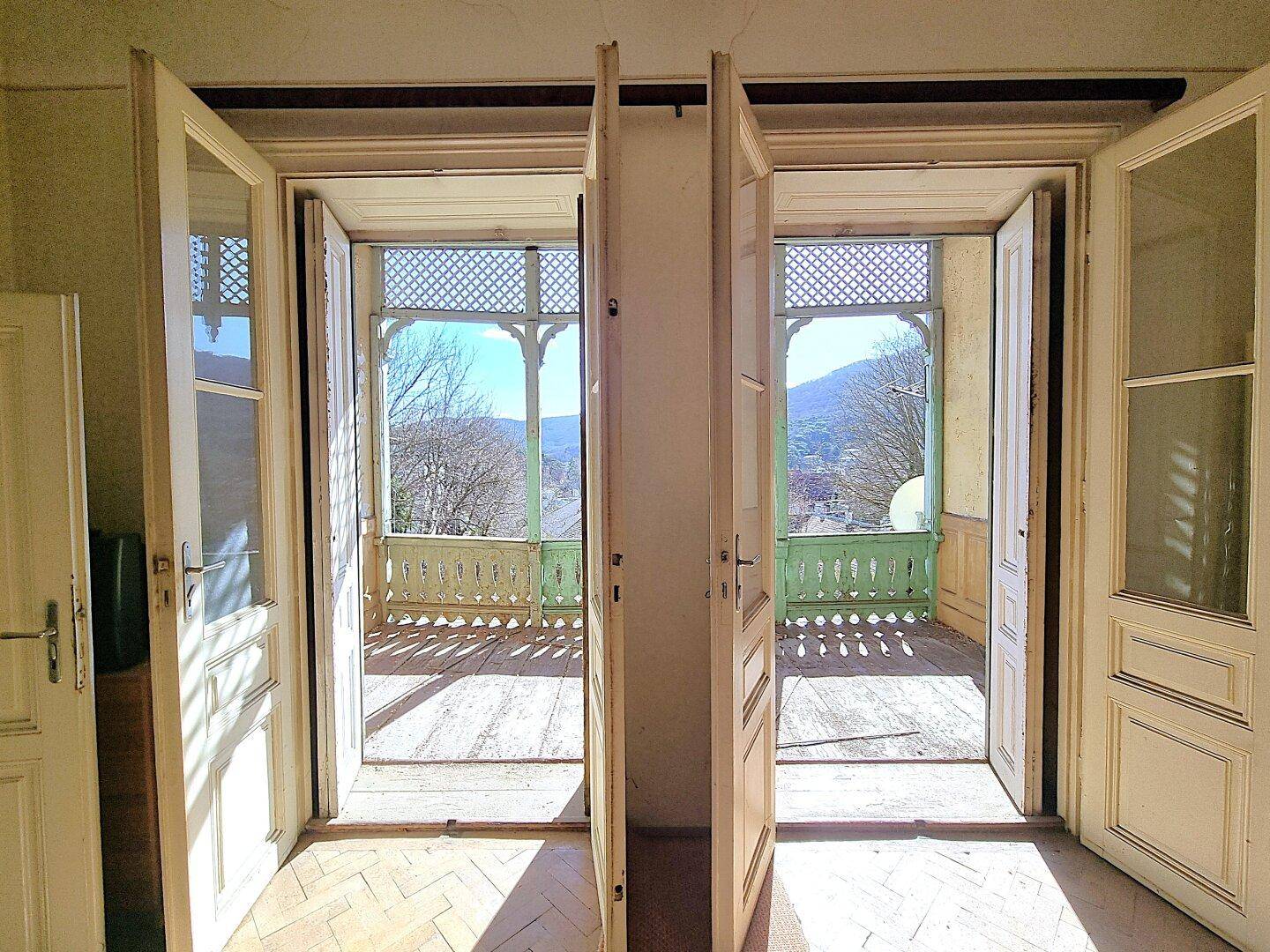 Offene Balkontüren mit Blick auf die umliegende Landschaft und Berge, heller Innenraum.