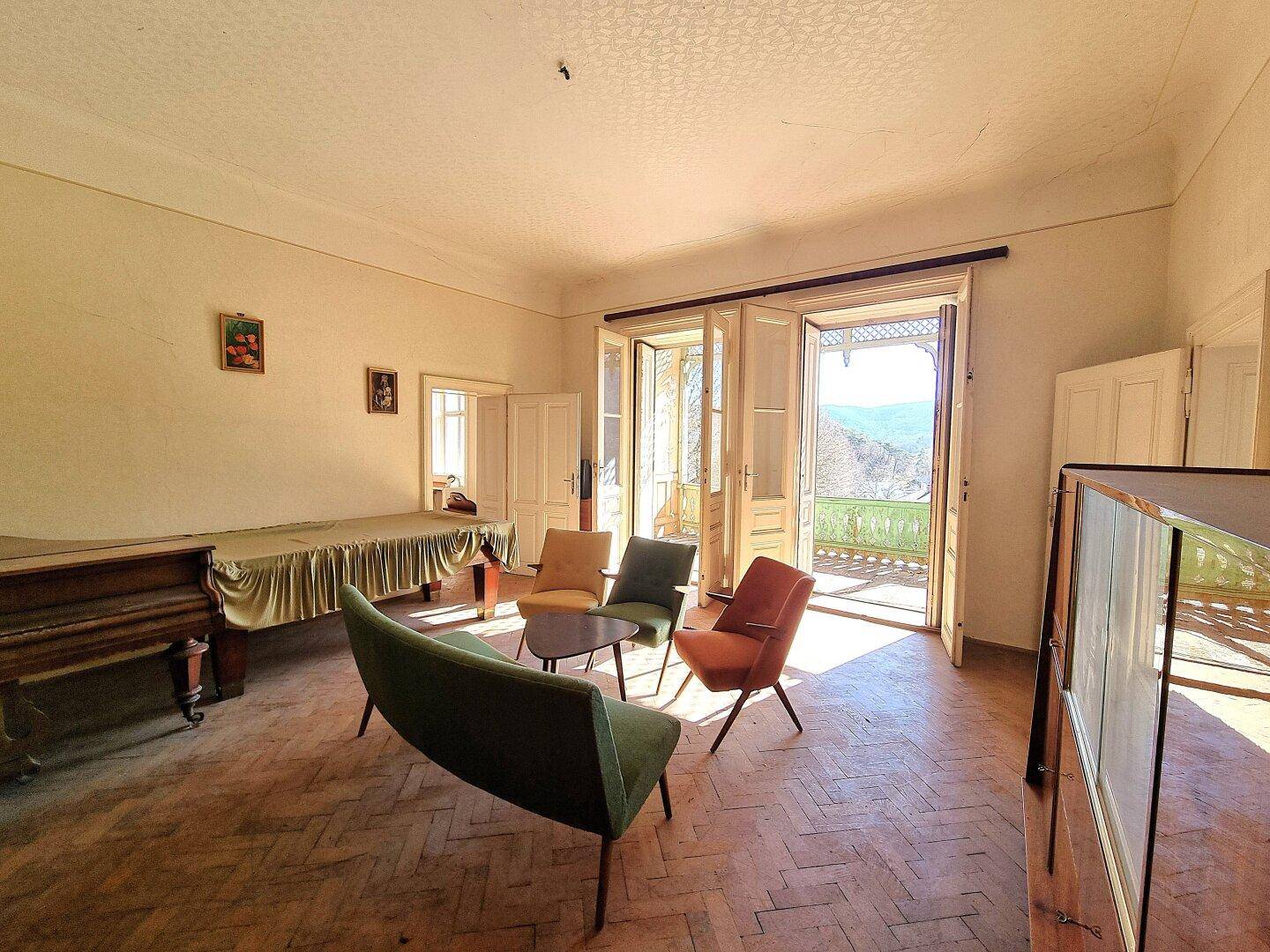 Geräumiges Wohnzimmer mit Fischgrätparkett, bunten Möbeln und Zugang zum Balkon mit Weitblick.
