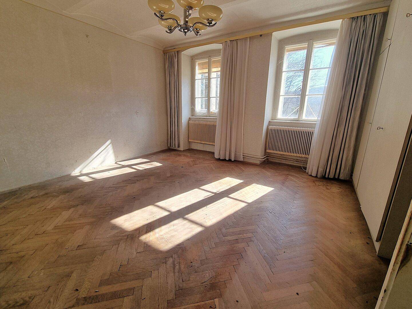 Helles Zimmer mit Fischgrätparkett, hohen Fenstern und Heizkörpern, sonnendurchflutet.
