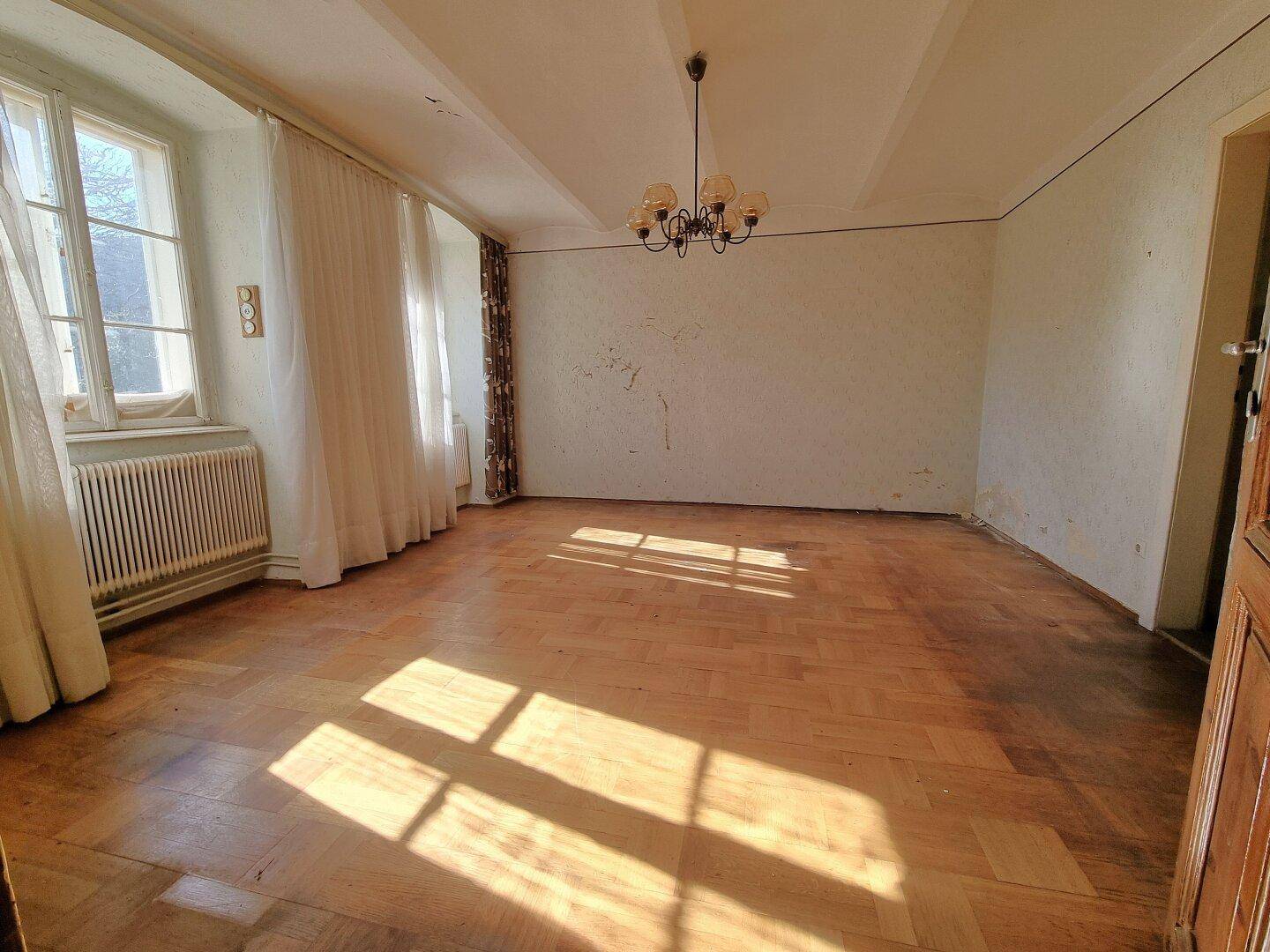 Geräumiges Zimmer mit Fischgrätparkett und hohen Decken, hell durch große Fenster.