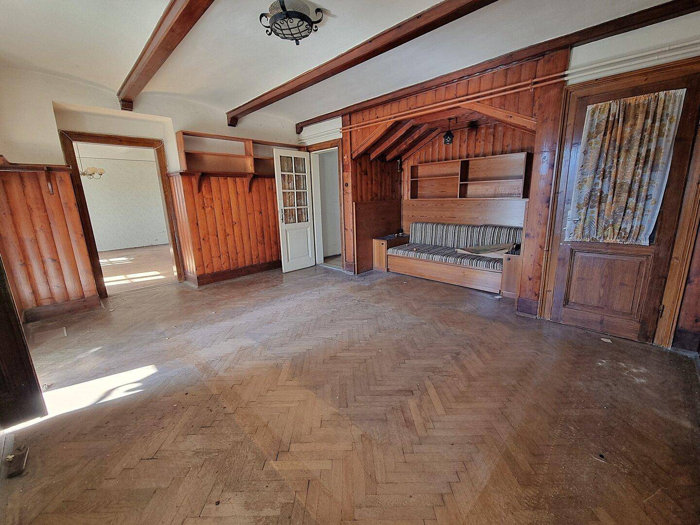 Rustikales Wohnzimmer mit Holzvertäfelung, Holzbalken und Fischgrätparkett, gemütliche Atmosphäre.