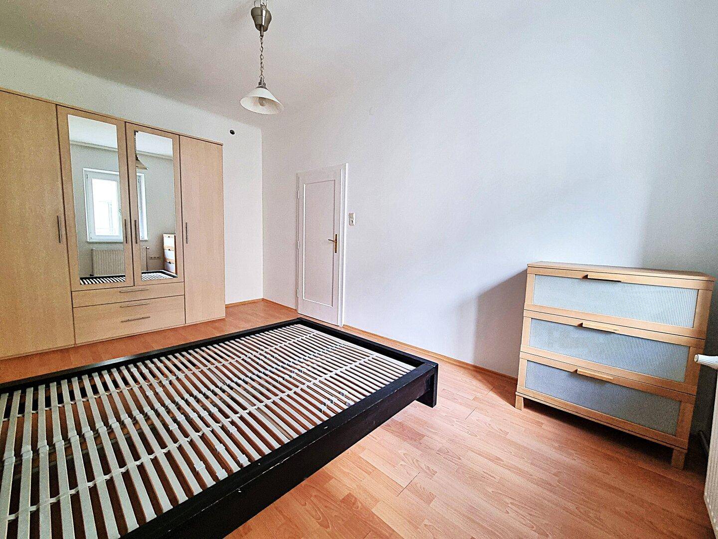 Geräumiges Schlafzimmer mit Bettrahmen, Kommode und großem Spiegelschrank, bietet viel Stauraum.