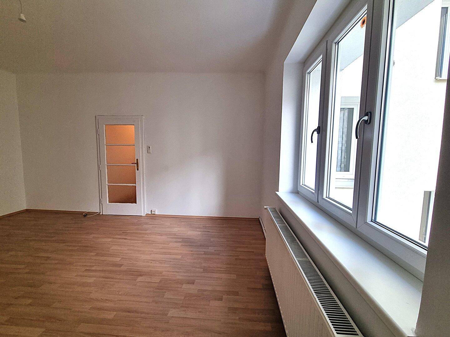 Geräumiges Zimmer mit großen Fenstern und Heizkörper, bietet viel Tageslicht und eine neutrale Basis.