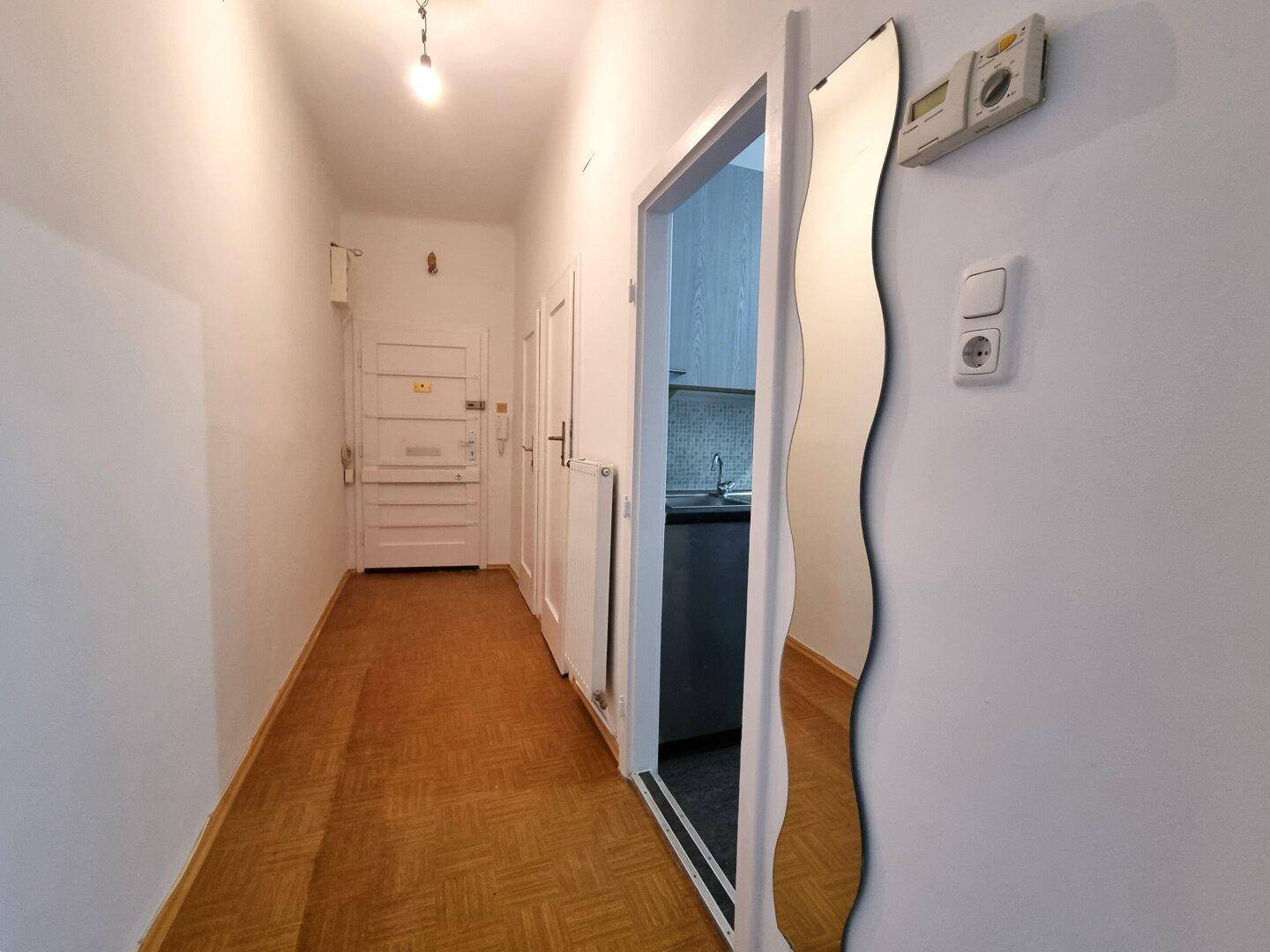 Langer Flur mit Parkettboden und mehreren Türen, ein dekorativer Spiegel schmückt die Wand.