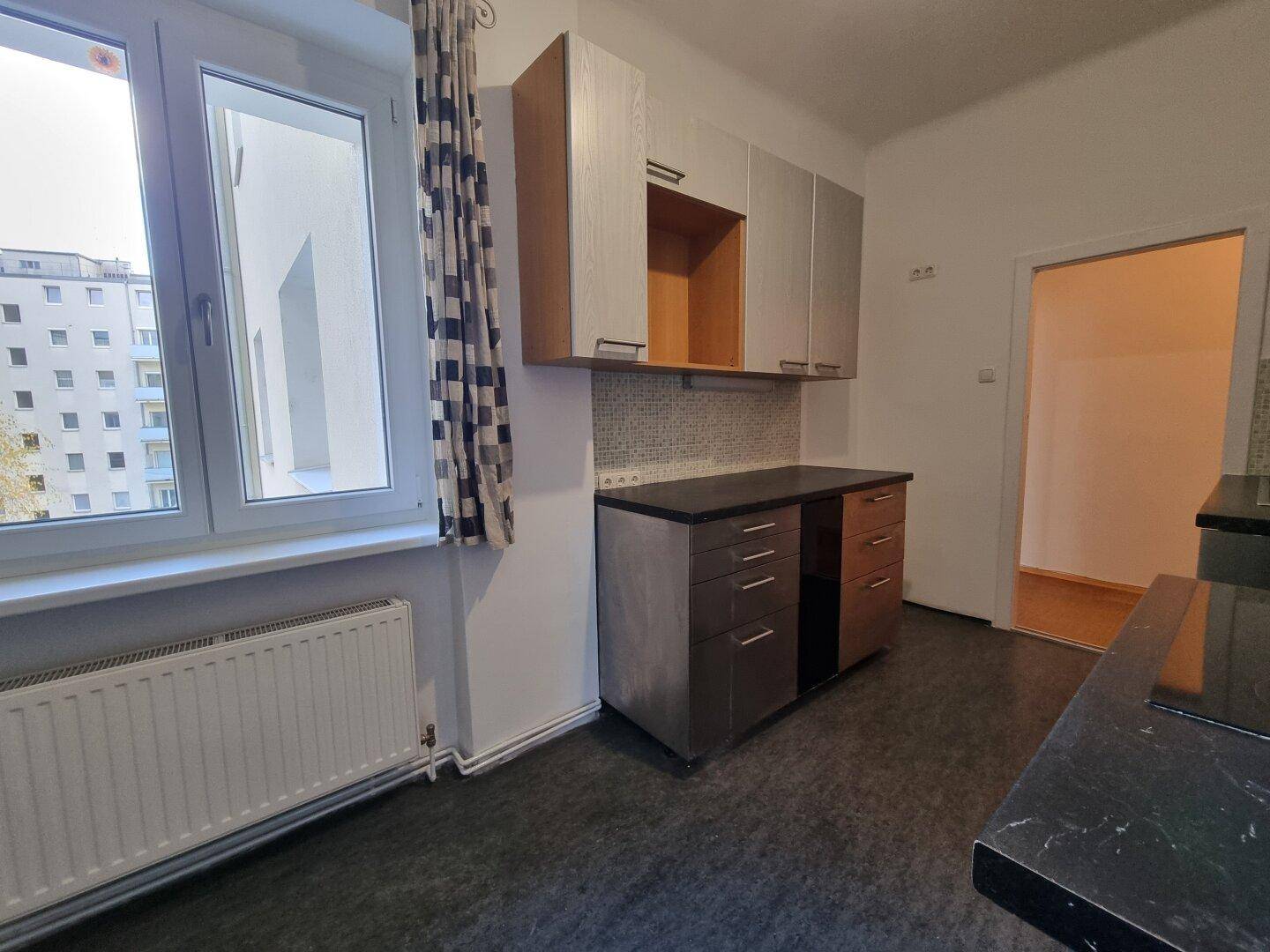 Helle Küche mit Fenster, Vorhängen und ausreichend Arbeitsfläche, bietet einen Blick nach draußen.