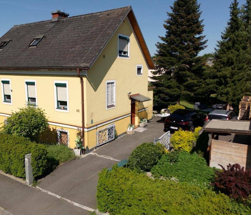 Gelbes Haus mit Einfahrt, gepflegtem Vorgarten und parkenden Autos.