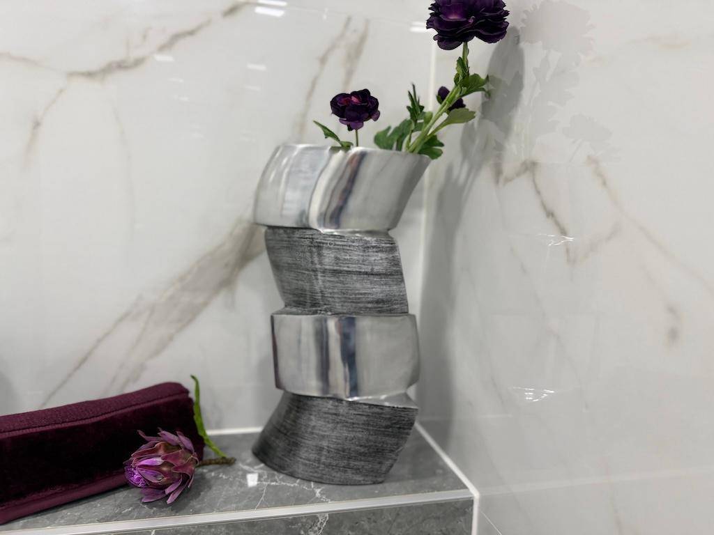 Dekorative Vase mit Blumen auf einer Marmorablage in einem modern gefliesten Badezimmer.