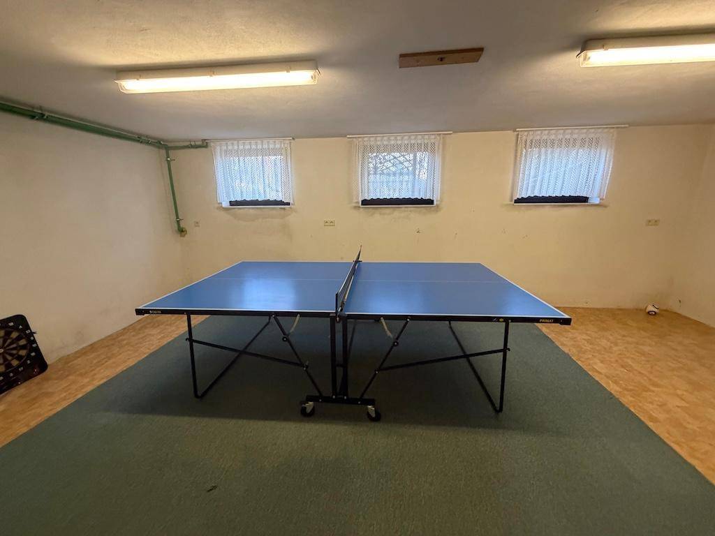 Großer Kellerraum mit Tischtennisplatte und kleinen Fenstern, ideal für Freizeitaktivitäten.