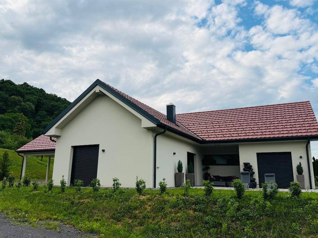 Freistehendes Einfamilienhaus mit rotem Dach und weißer Fassade, umgeben von grüner Hügellandschaft.