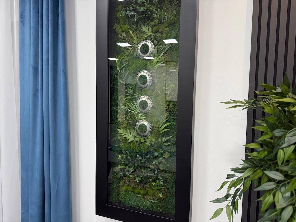 Detailaufnahme einer vertikalen Pflanzenwanddekoration mit grünen Blättern und silbernen Akzenten.