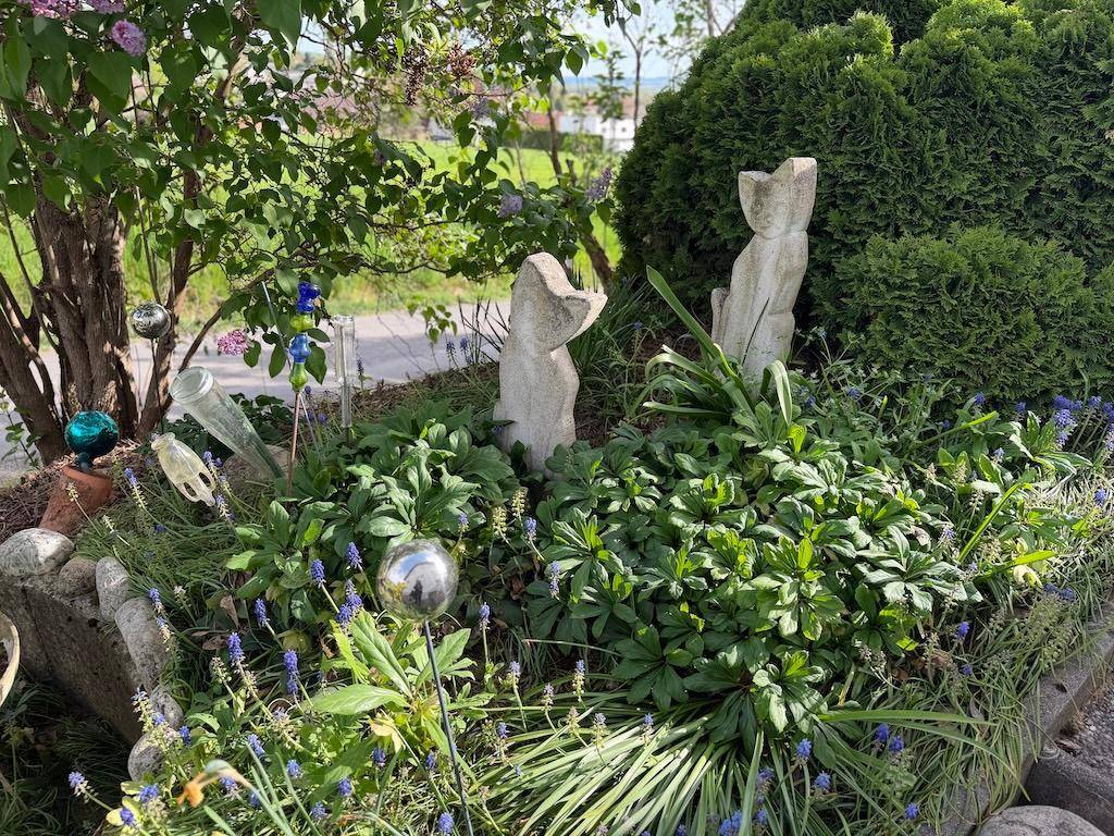 Detailansicht eines Gartens mit dekorativen Statuen, üppigen Pflanzen und einem kleinen Baum.