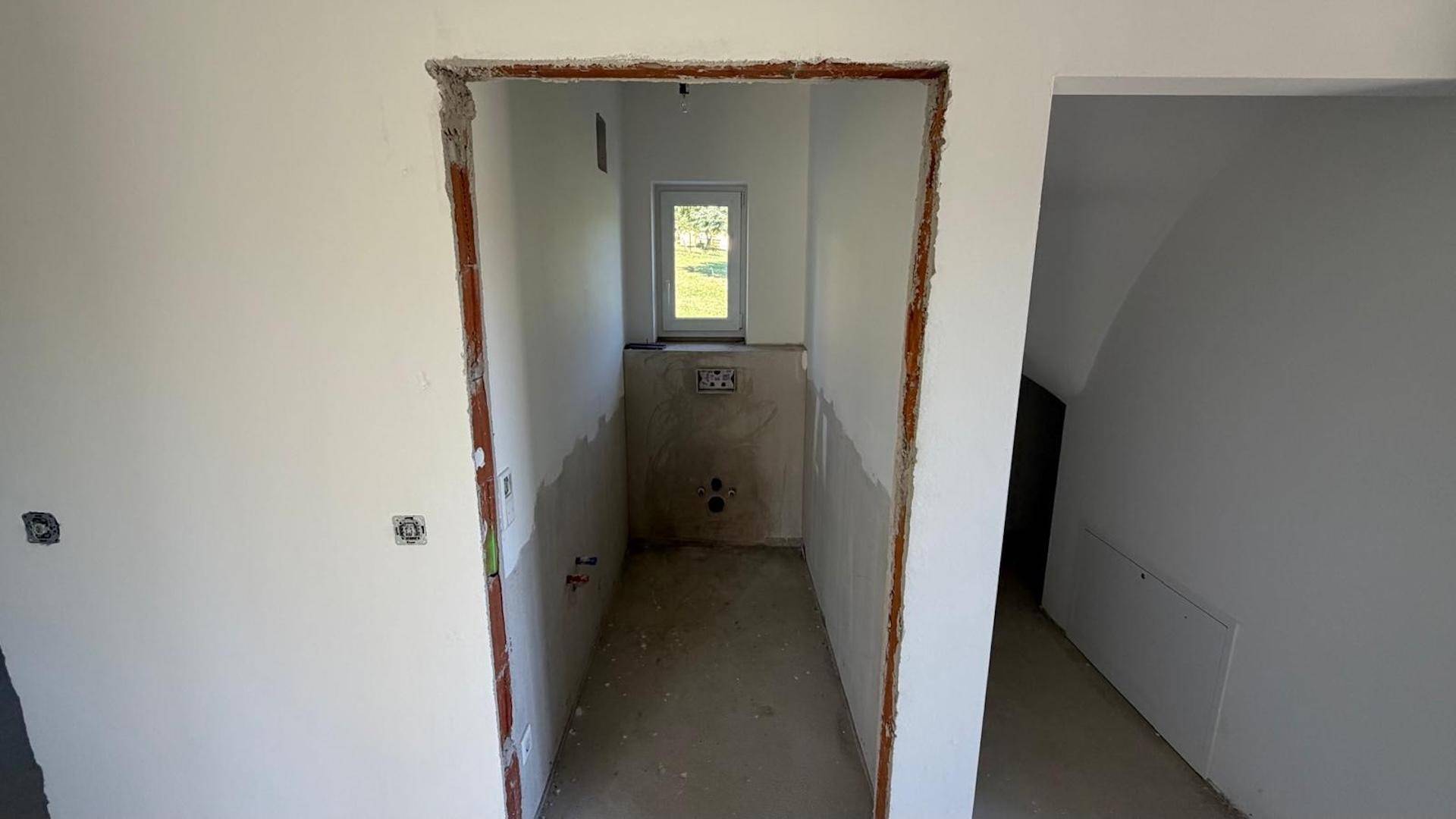 Unfertiger WC-Raum mit Fenster und vorbereiteten Anschlüssen für die Sanitäreinrichtung.