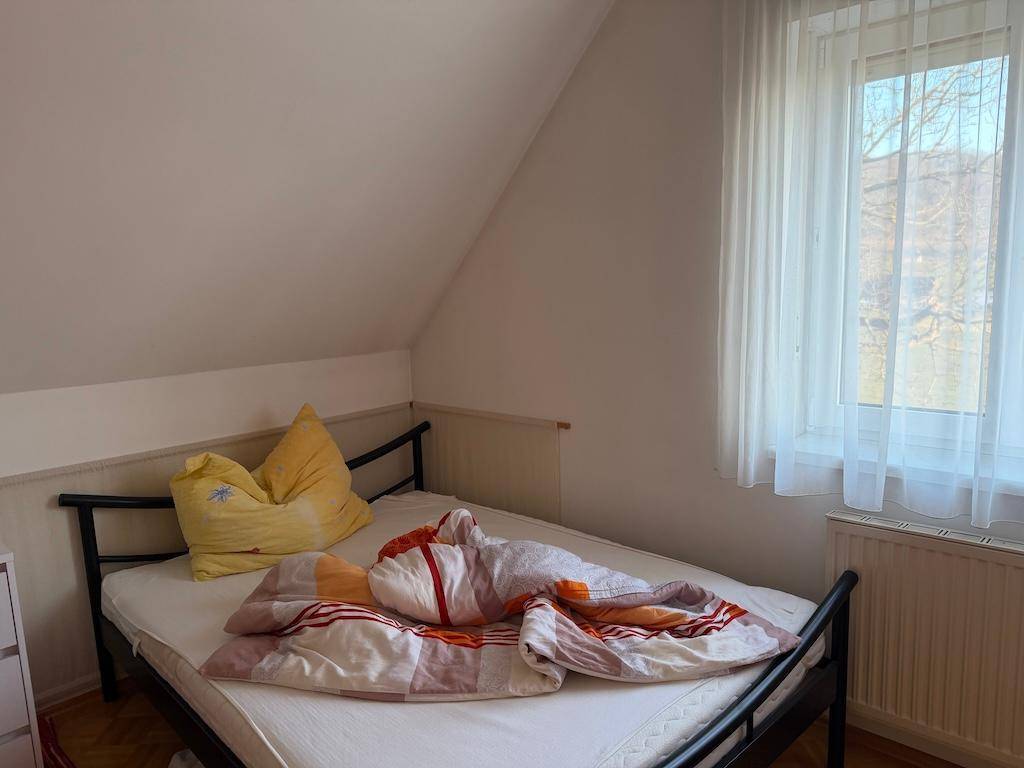 Gemütliches Schlafzimmer mit Einzelbett, Dachschräge und Fenster, einfach eingerichtet.