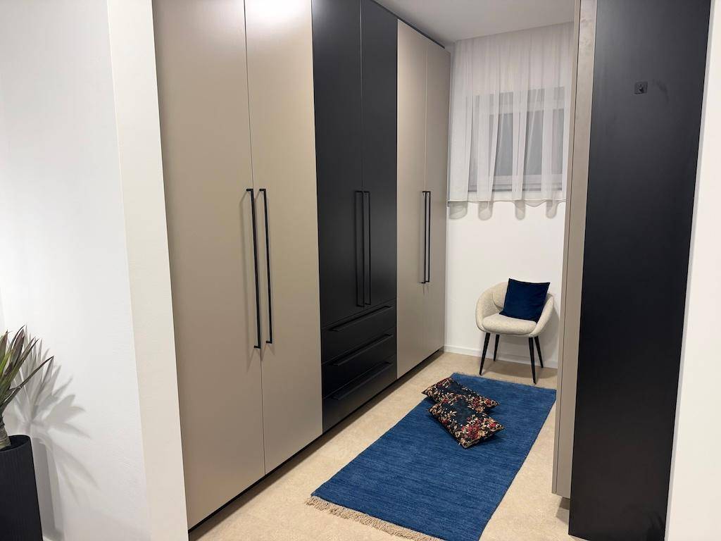 Ankleidebereich im Schlafzimmer mit Einbauschränken, Teppich und einem kleinen Sessel.