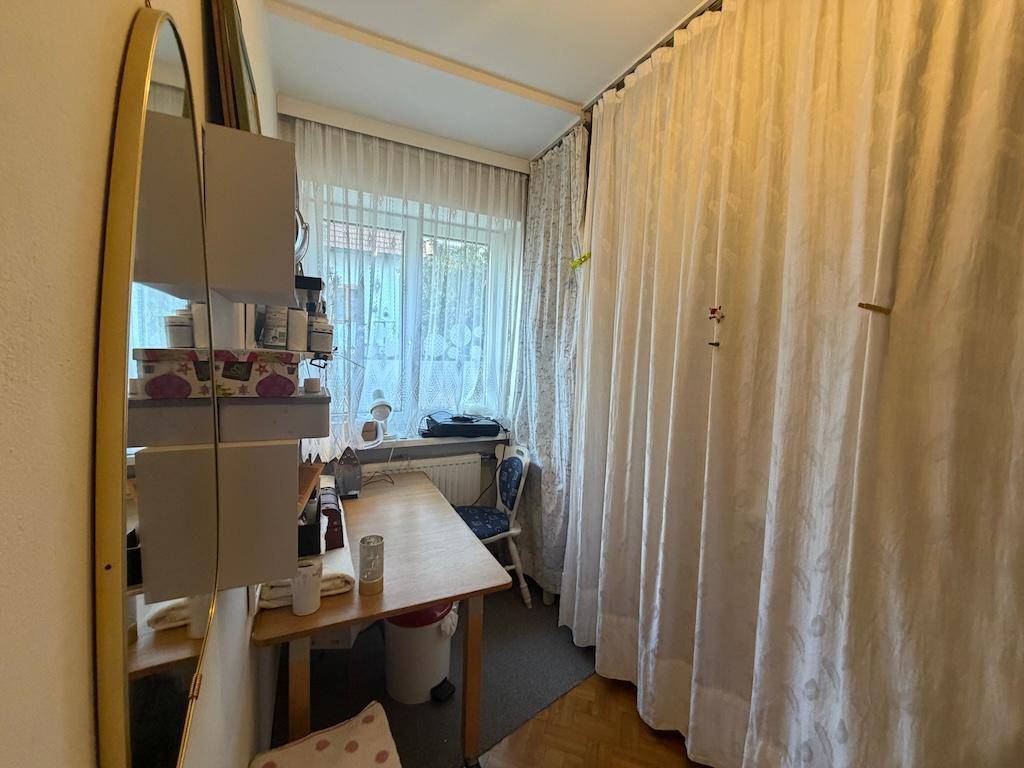 Kleines Arbeitszimmer mit Schreibtisch, Fenster und Vorhängen, funktional eingerichtet.