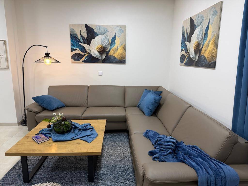 Modernes Wohnzimmer mit beigem Ecksofa, Stehlampe und dekorativen Bildern an der Wand.