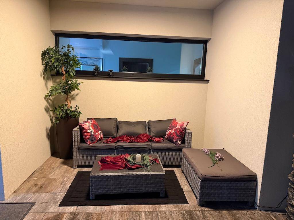 Komfortabler Außenwohnbereich mit Rattanmöbeln, Sofa und dekorativen Kissen.