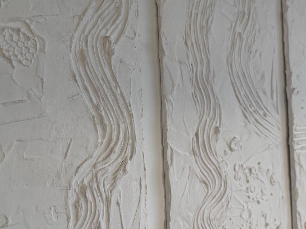 Nahaufnahme einer strukturierten weißen Wand mit wellenförmigen Mustern, dekorativ gestaltet.