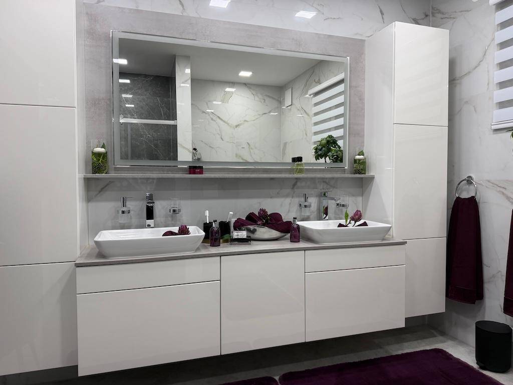 Elegantes Badezimmer mit Doppelwaschbecken, großem Spiegel und modernen weißen Schränken.