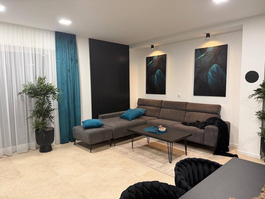 Helles Wohnzimmer mit einem bequemen Ecksofa, grünen Pflanzen und modernen Wanddekorationen.