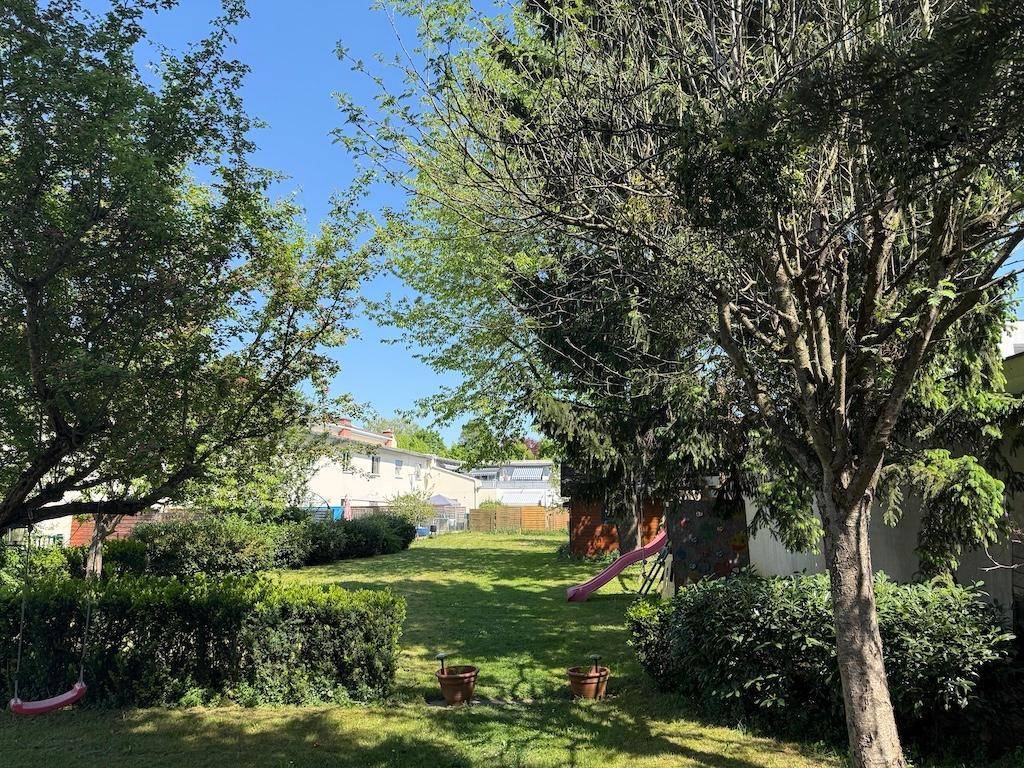 Weitläufiger grüner Garten mit Rasen, Bäumen, Hecken und Kinderspielgeräten.