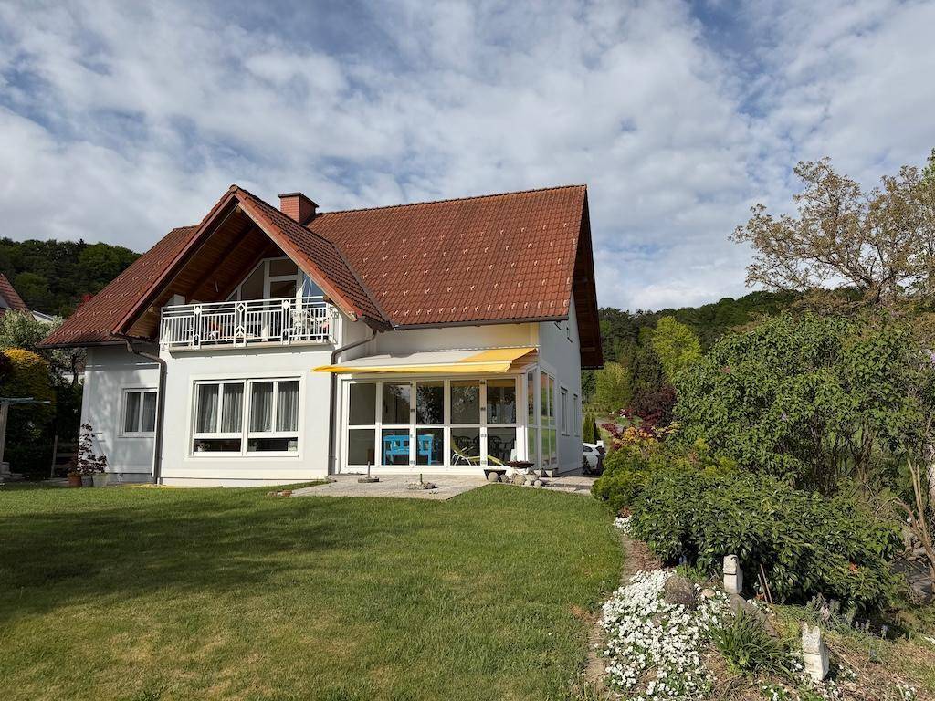 Ansicht des Hauses vom Garten aus, mit rotem Ziegeldach und grüner Umgebung.
