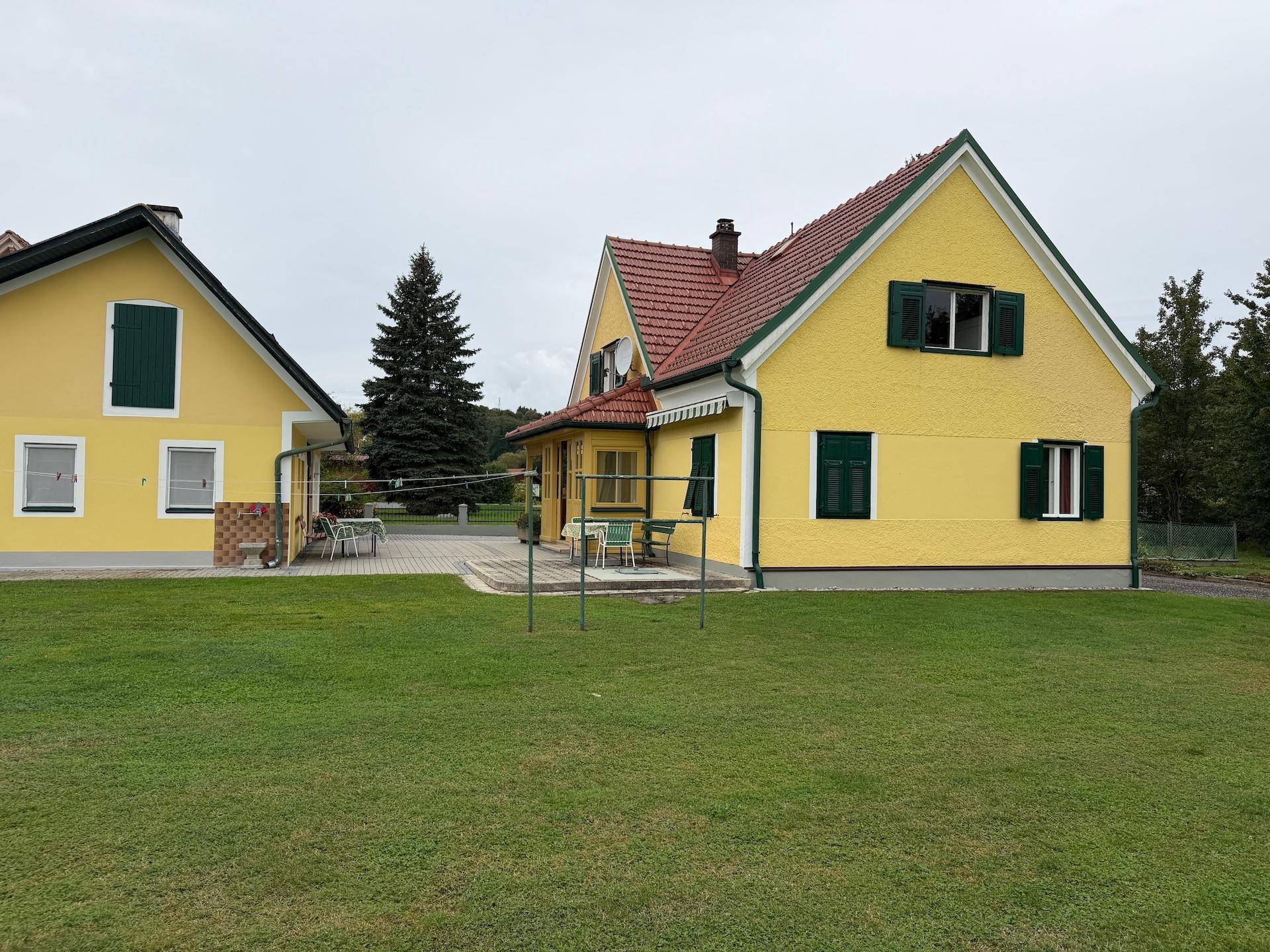 Seitenansicht des Hauses mit gelber Fassade, grünen Fensterläden und einem gepflegten Rasenbereich.
