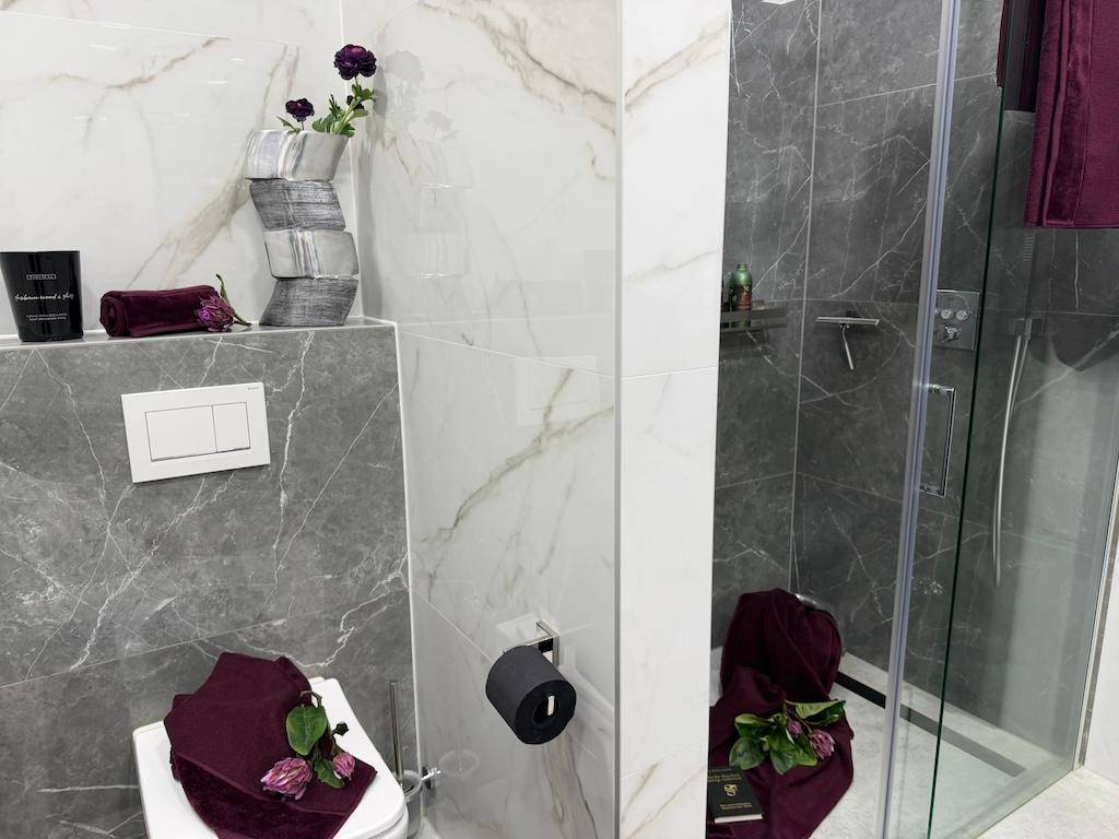 Modernes Badezimmer mit eleganten Marmorfliesen, Toilette und einer geräumigen Duschkabine.