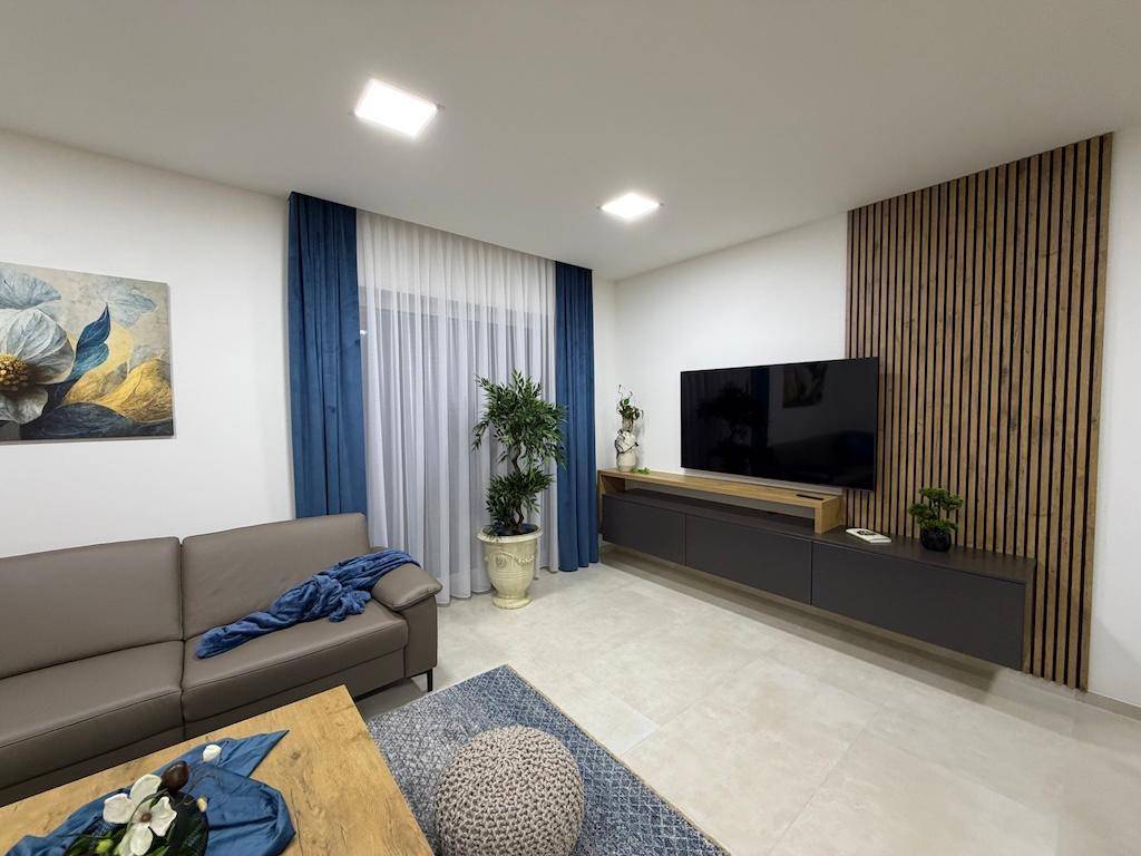 Modernes Wohnzimmer mit beigem Sofa, Holzwandverkleidung und großem Fernseher.