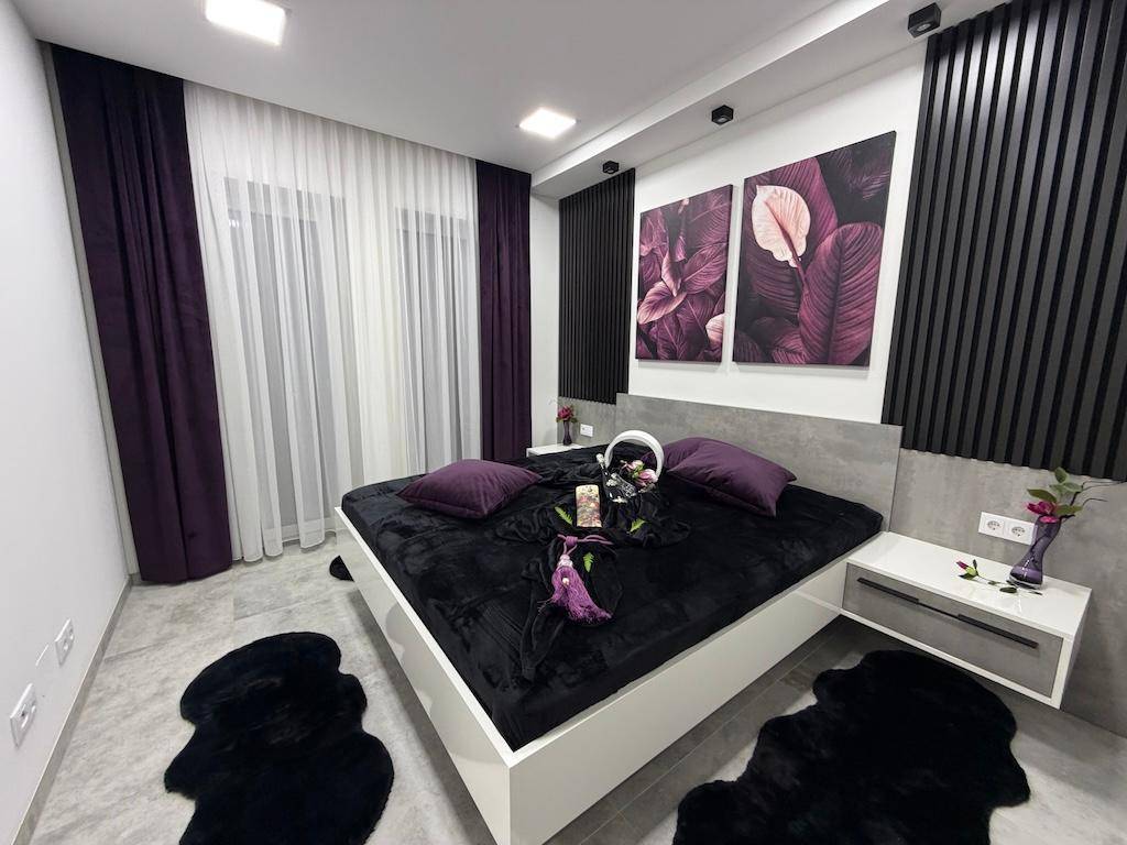 Elegantes Schlafzimmer mit dunklem Bett, lila Dekoration und indirekter Beleuchtung für eine gemütliche Stimmung.