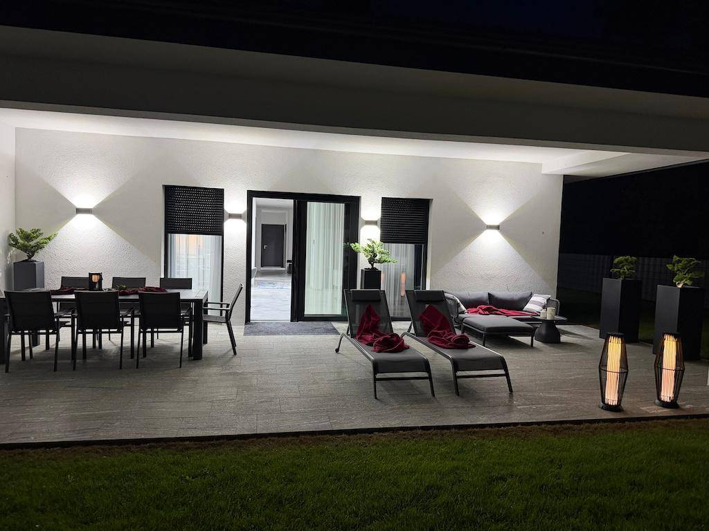 Großzügige, beleuchtete Terrasse am Abend mit Essbereich, Lounge-Möbeln und dekorativen Elementen.
