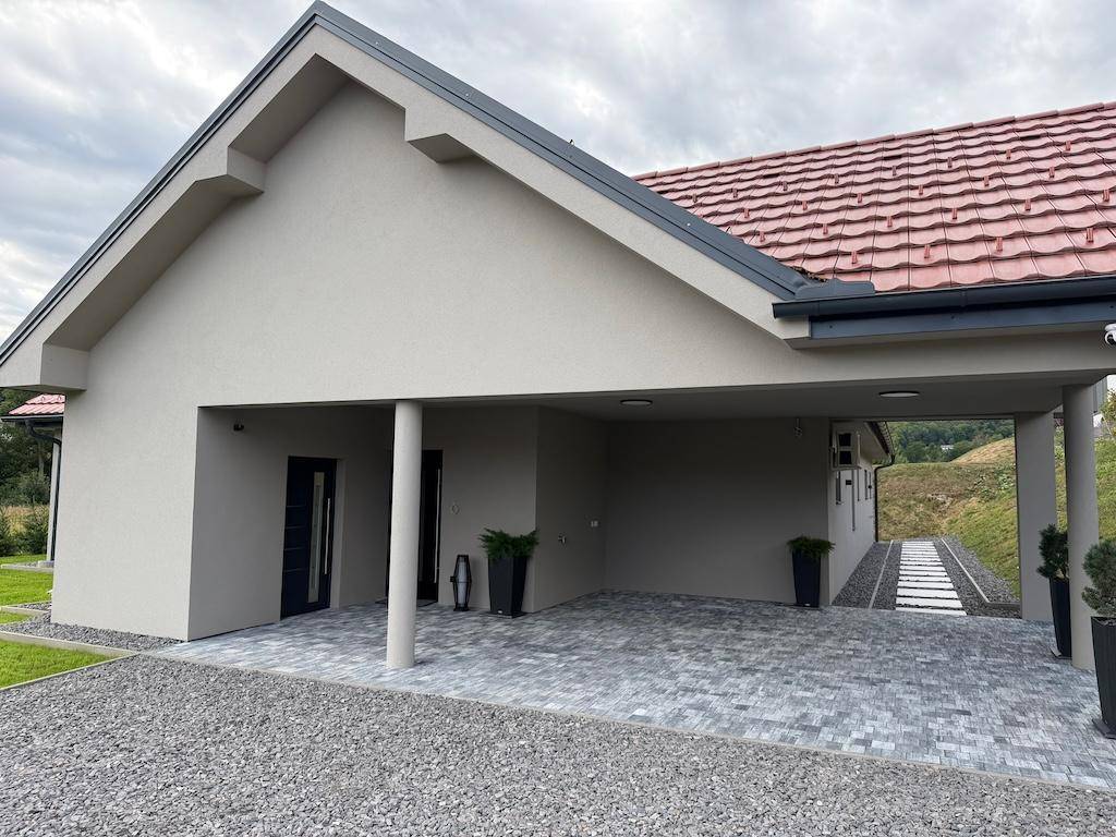 Ansicht des modernen Einfamilienhauses mit Carport und gepflegtem Vorgarten unter bewölktem Himmel.