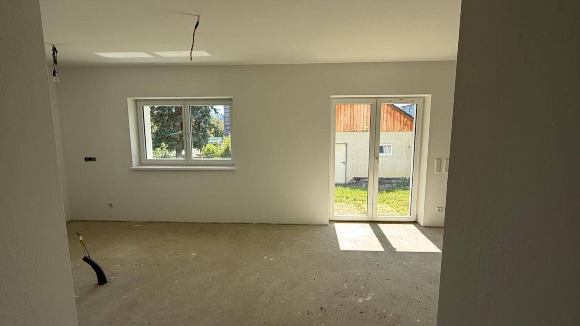 Geräumiger Wohnbereich im Rohbau mit großen Glastüren und Blick auf den zukünftigen Garten.