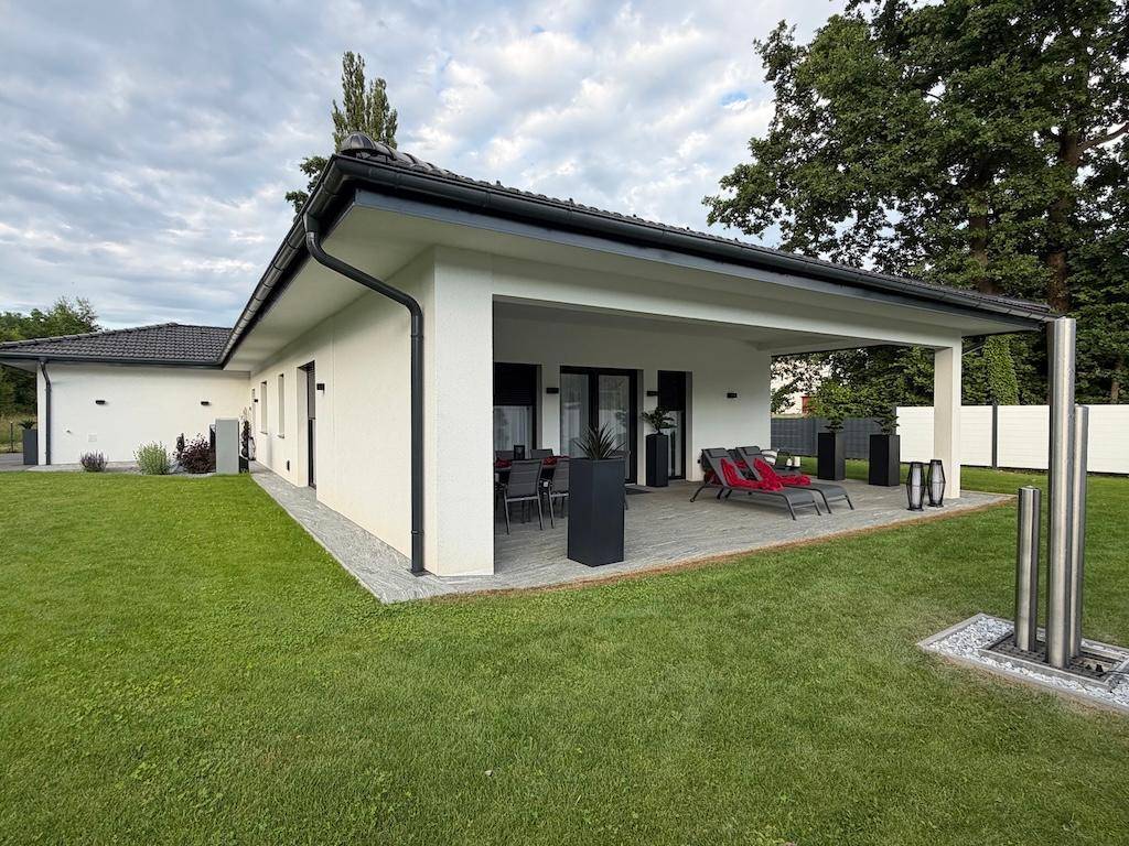 Modernes Einfamilienhaus mit weitläufigem Rasen und großer überdachter Terrasse, umgeben von viel Grün.