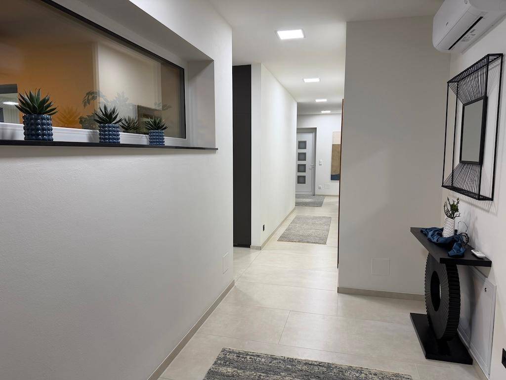 Langer, heller Flur mit modernen Fliesen, einem schmalen Fenster und dekorativen Pflanzen.
