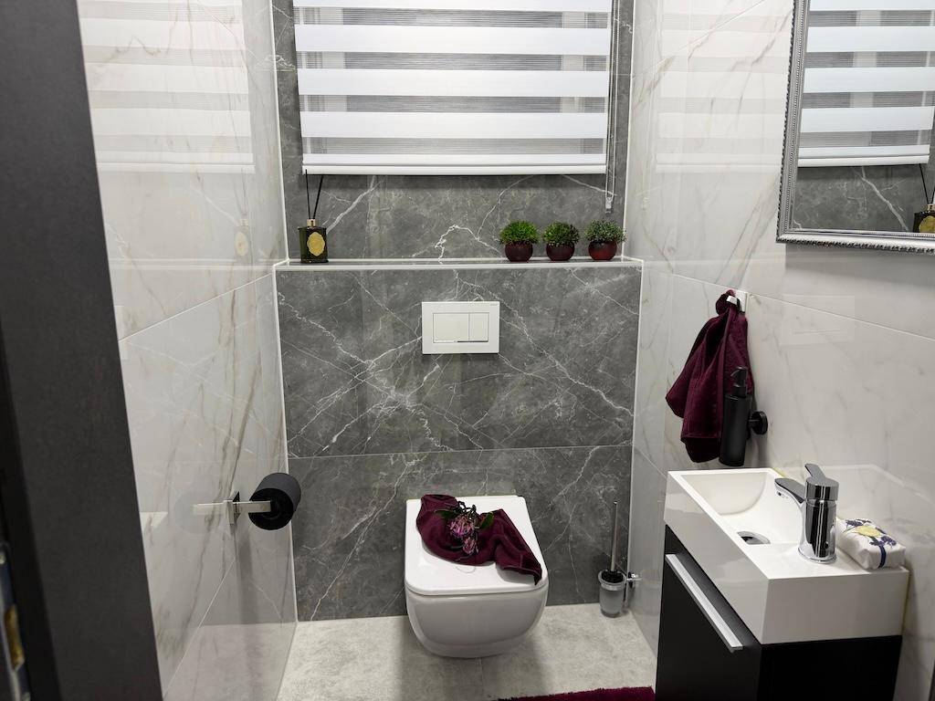 Modernes Gäste-WC mit eleganten grauen Marmorfliesen, wandhängendem WC und kleinem Waschbecken.