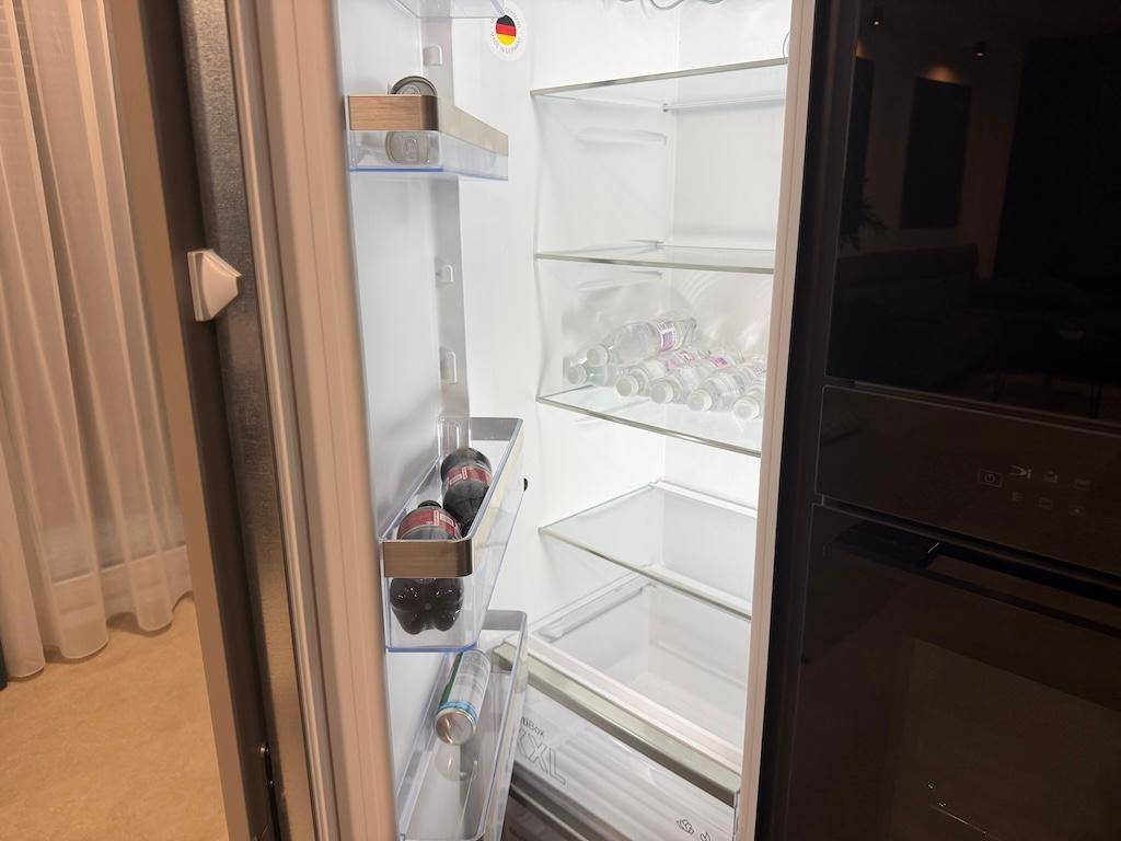 Ein geöffneter Kühlschrank mit Glasablagen und einigen Getränken, sauber und modern.
