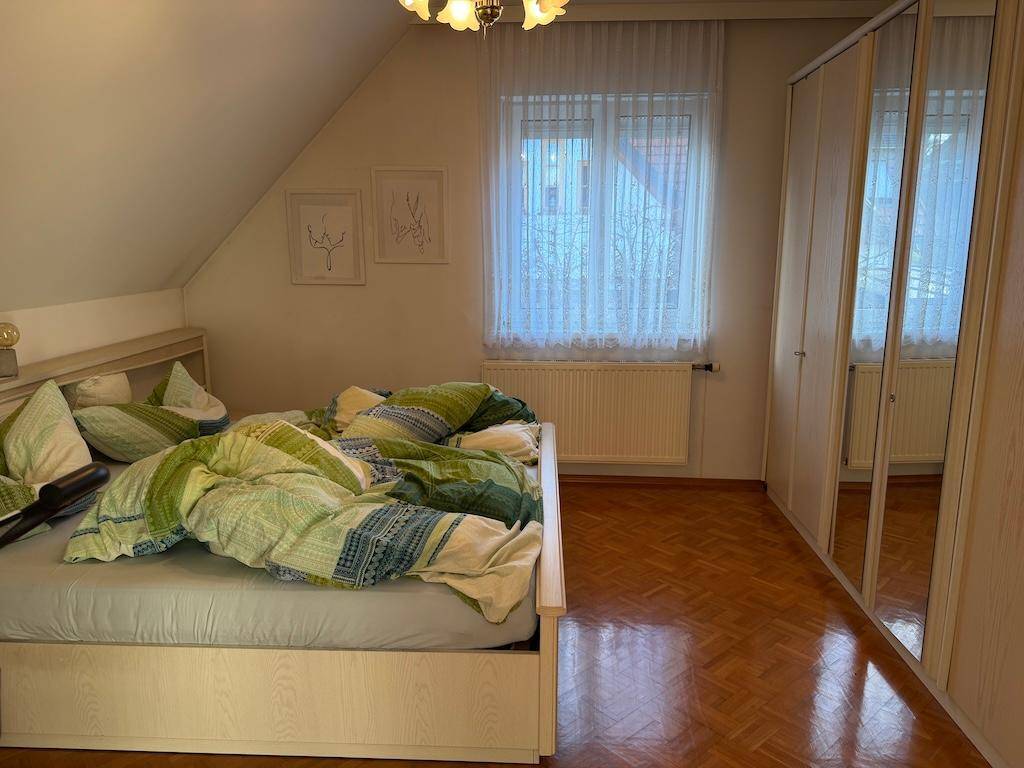 Schlafzimmer mit Doppelbett, Spiegelschrank, Parkettboden und Fenster, hell und geräumig.