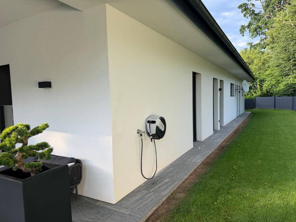 Seitenansicht des Hauses mit gepflegtem Rasen, Steinweg und einer Ladestation für Elektrofahrzeuge.