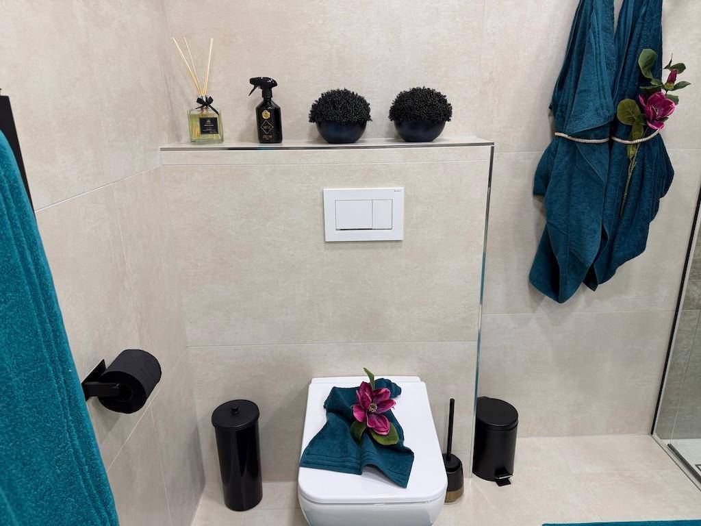 Modernes WC mit beigefarbenen Fliesen, schwarzem Zubehör und tealfarbenen Handtüchern.