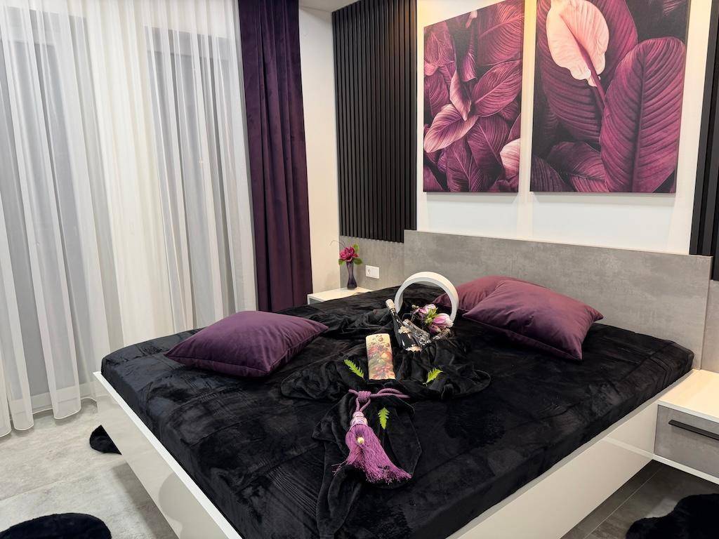 Gemütliches Schlafzimmer mit großem Bett, lila Kissen und moderner Wanddekoration in warmen Farbtönen.