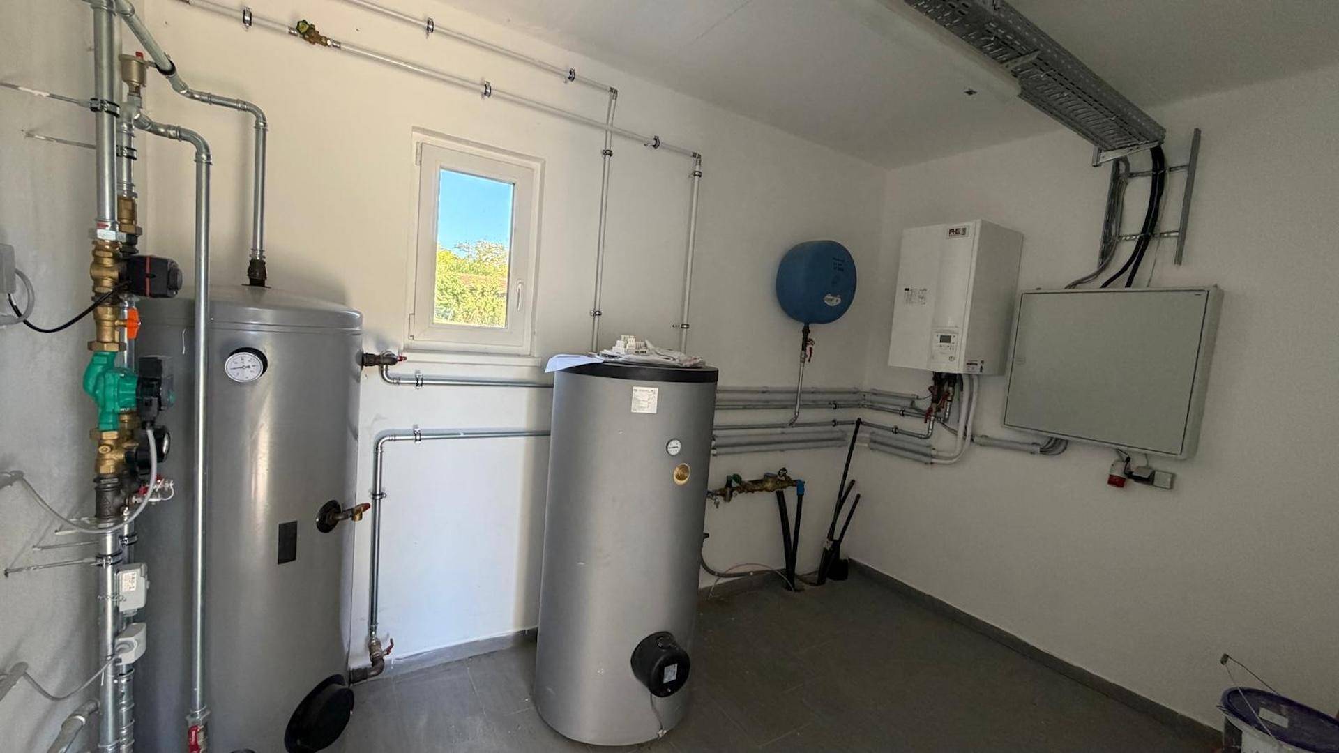 Technikraum mit Heizungsanlagen, Warmwasserspeichern und einem Fenster für Belüftung und Tageslicht.