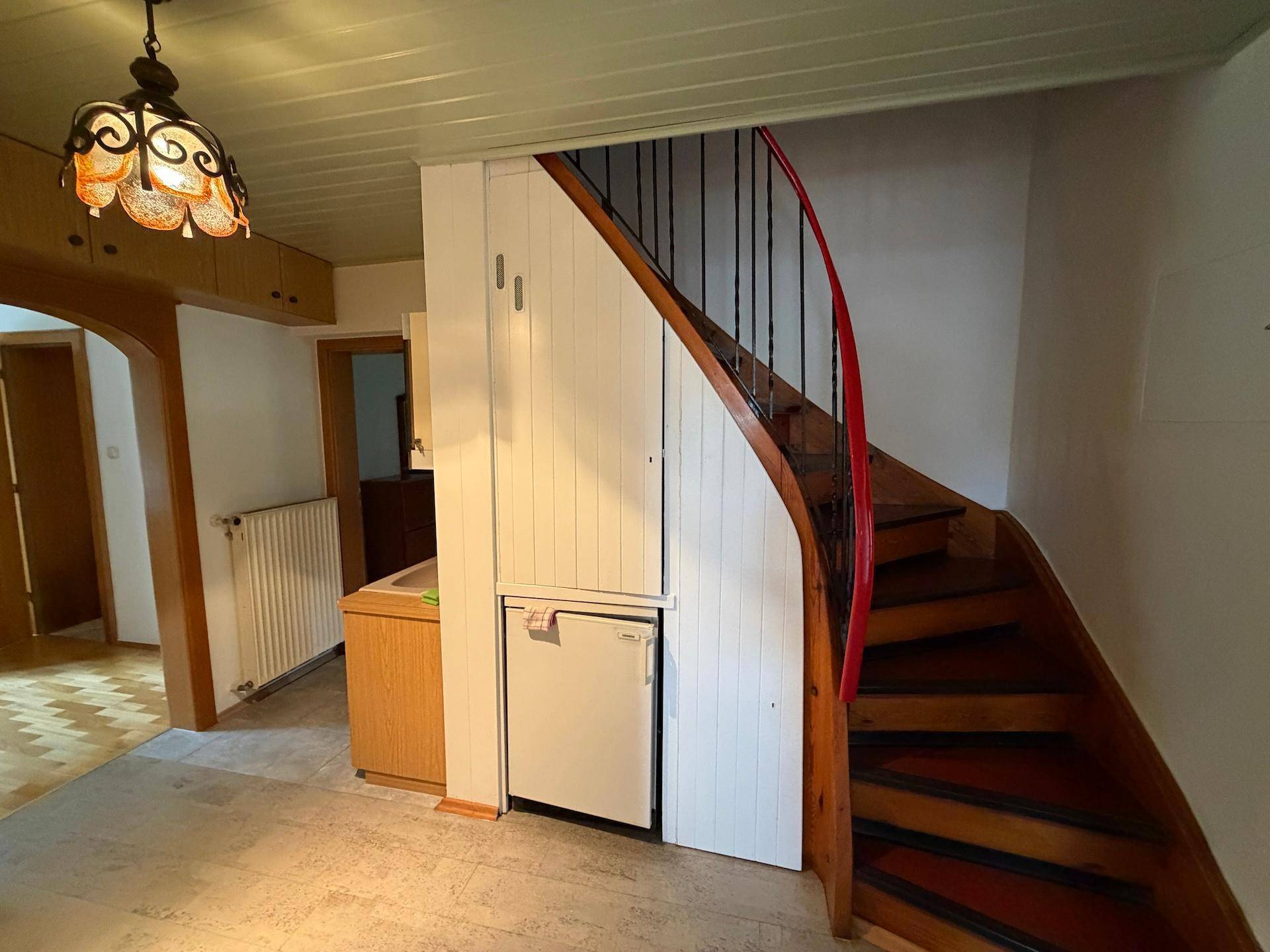 Heller Eingangsbereich mit Holztreppe und weiß getäfelten Wänden, der zu den oberen Etagen führt.