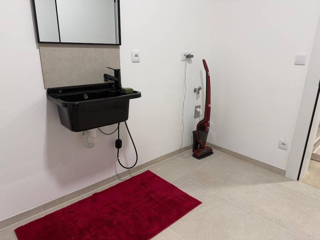 Funktionaler Hauswirtschaftsraum mit schwarzem Waschbecken, Spiegel und Fliesenboden.